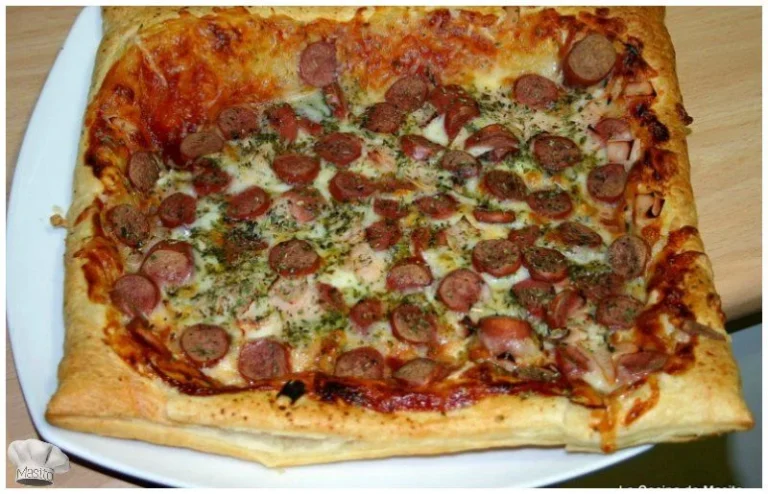 Pizza de hojaldre con pavo y salchichas, cubierta con queso fundido y especias, horneada hasta quedar dorada y crujiente. Receta de pizza de hojaldre con salchichas de La cocina de Masito