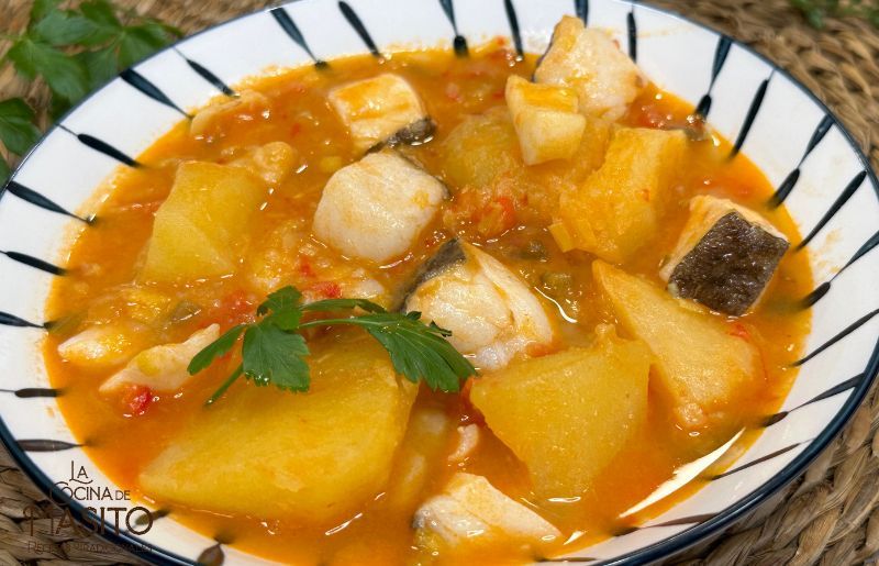 Patatas con sepia y bacalao servidas en un plato hondo, con un toque de perejil fresco y salsa casera.