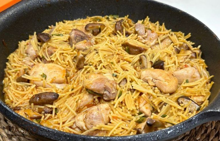 Plato de fideuá de pollo con setas shitake, servido en una paellera con un toque de perejil fresco.