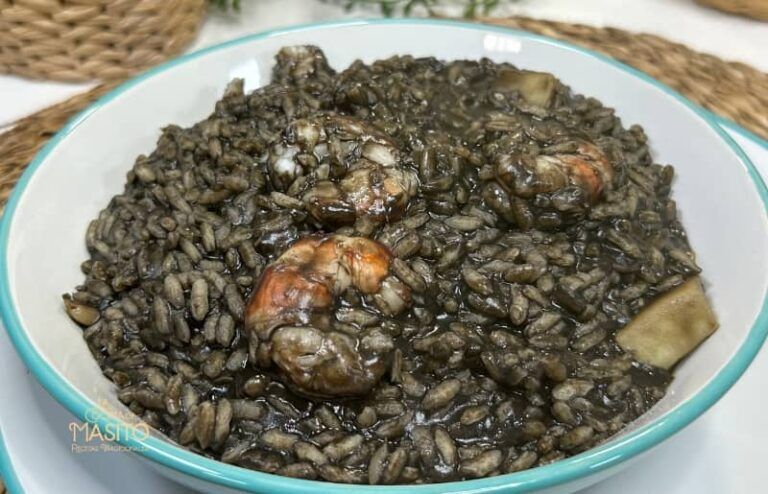 Plato de arroz negro meloso acompañado de trozos de sepia y langostinos frescos, decorado con perejil fresco.