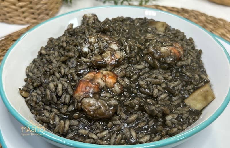 Plato de arroz negro meloso acompañado de trozos de sepia y langostinos frescos, decorado con perejil fresco.