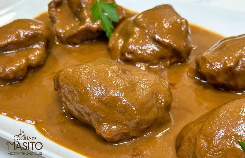 Carrilleras en salsa de chocolate servidas en un plato elegante con un fondo oscuro.
