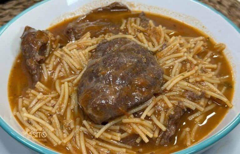 Plato de cazuela de fideos con carrilleras de cerdo servido en una fuente de barro, acompañado de hierbas frescas.