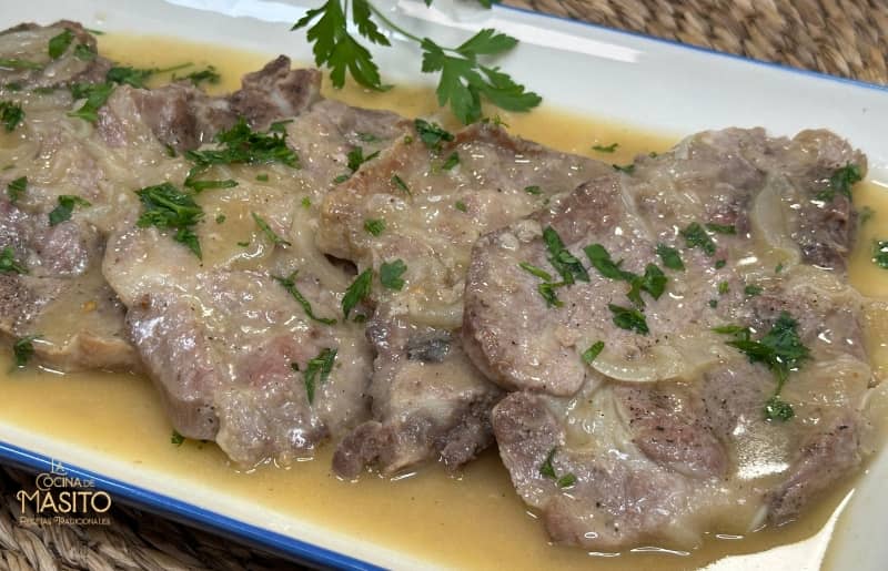 Chuletas de cerdo doradas en una cremosa salsa de cebolla casera, servidas en un plato rústico.