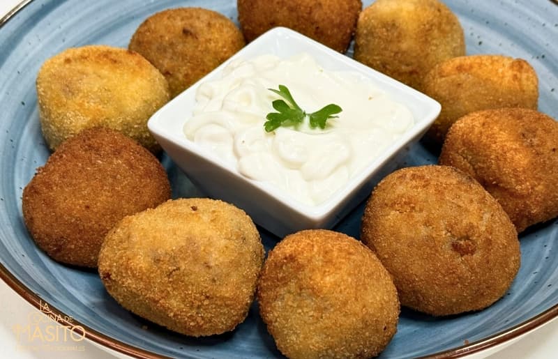 Croquetas doradas y cremosas de carrilleras de ternera sobre un plato de cerámica con perejil fresco como decoración.