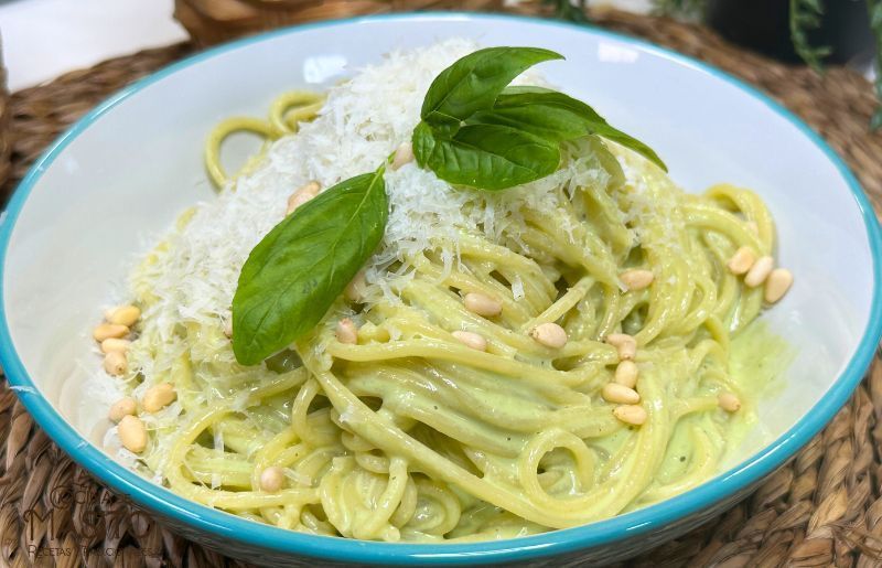 Plato de espaguetis en salsa pesto servido con albahaca fresca y queso parmesano rallado.