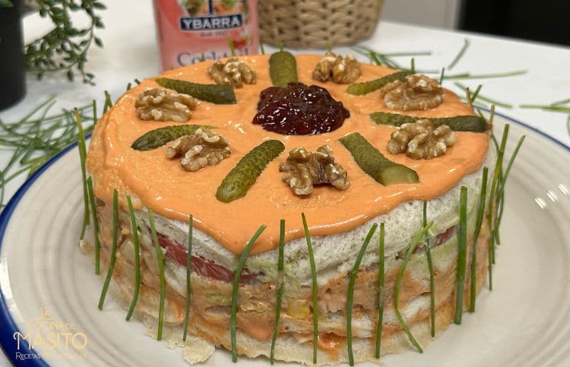 Pastel frío de pollo con pan de molde, decorado con salsa cocktail y vegetales frescos.