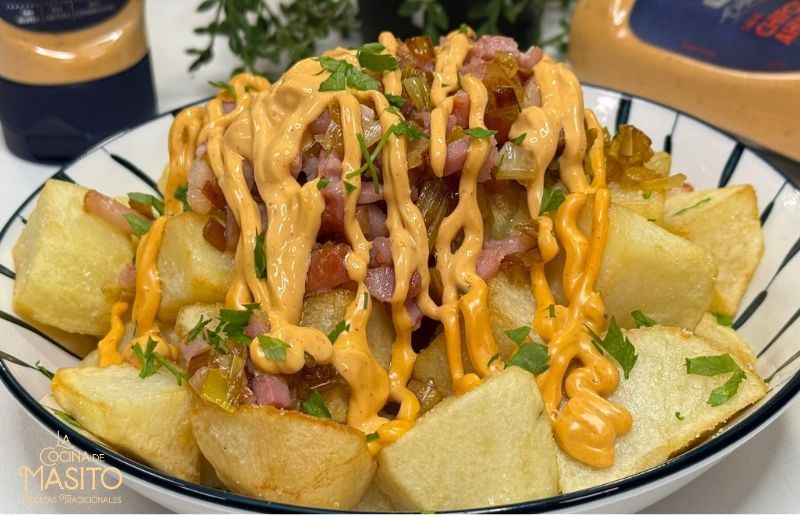 Patatas crujientes con bacon dorado y una cremosa salsa de chipotle ahumado servidas en un plato blanco.
