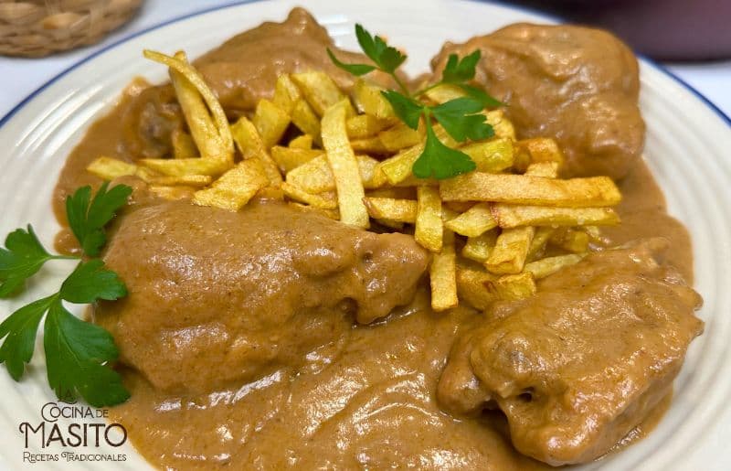 "Pollo en salsa de setas y verduras servido en un plato blanco con una guarnición de hierbas frescas."