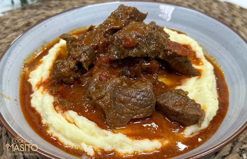 Fotografía de Pörkölt, un estofado húngaro tradicional servido en un plato con salsa espesa y acompañado de pan fresco.
