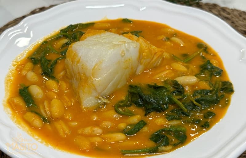 Un plato de potaje de alubias con espinacas y bacalao servido en un cuenco rústico, ideal para los días fríos.
