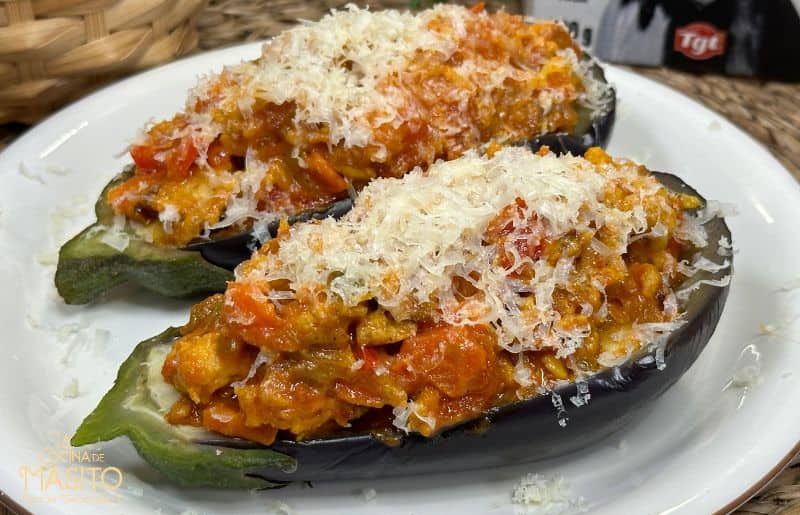 Berenjenas rellenas de carne de pollo gratinadas con queso, presentadas en un plato blanco con una decoración de perejil fresco