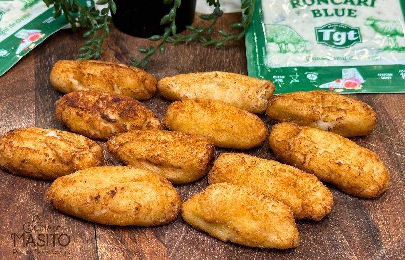 Croquetas doradas de atún y queso azul servidas en un plato con hojas frescas de perejil.
