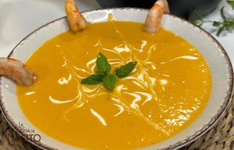 Crema de langostinos servida en un plato hondo, decorada con perejil fresco y trozos de langostino.