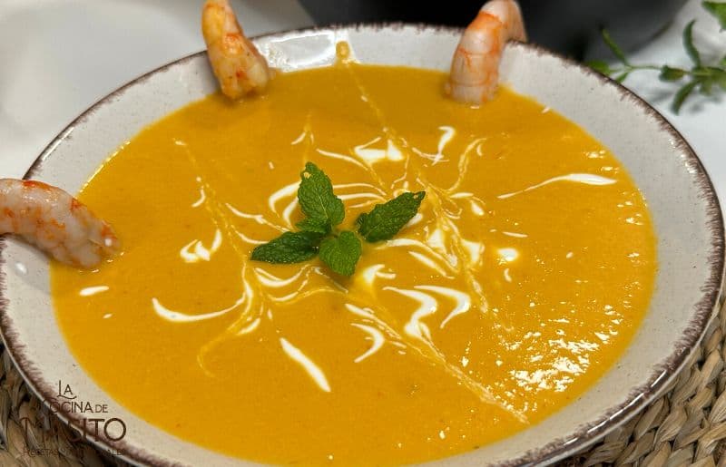 Crema de langostinos servida en un plato hondo, decorada con perejil fresco y trozos de langostino.