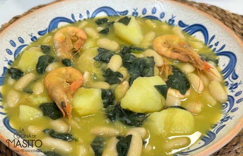 Imagen de un plato de fabes con calamares y gambas, acompañado de sartén y servido en una mesa rústica.