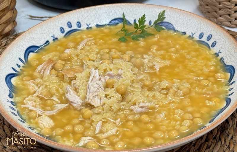 Plato de sopa de estrellas con pollo y garbanzos, servida caliente con caldo dorado y trozos de zanahoria.