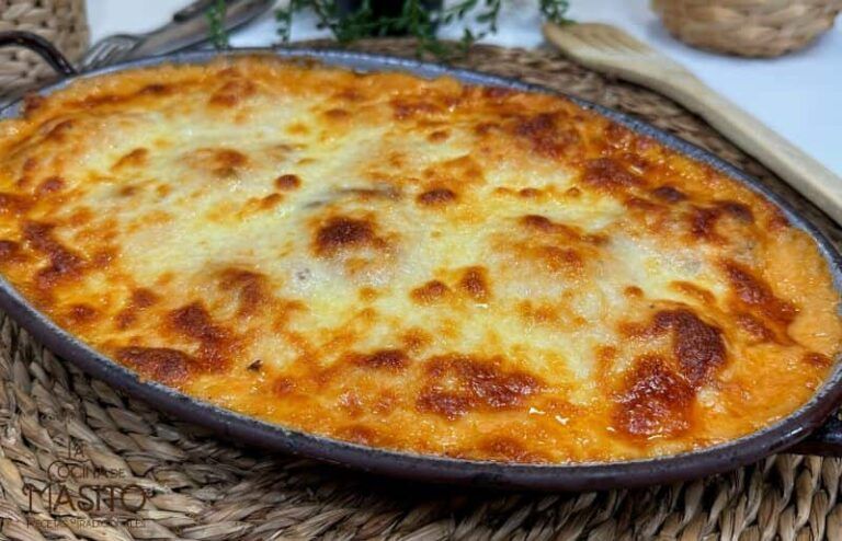 Huevos rellenos cubiertos con una cremosa salsa bechamel y decorados con pimientos caramelizados en un plato blanco.