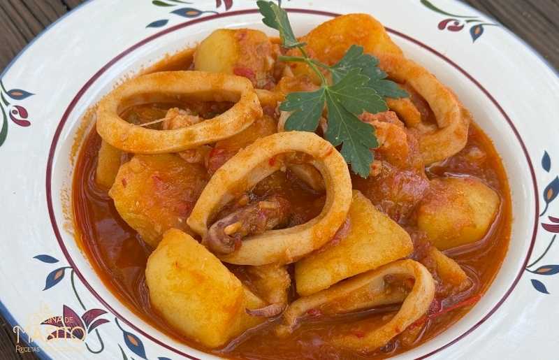 Primer plano de un plato de patatas guisadas con calamares y gambas, con una salsa espesa y dorada, servido en un cuenco de cerámica sobre una mesa rústica.