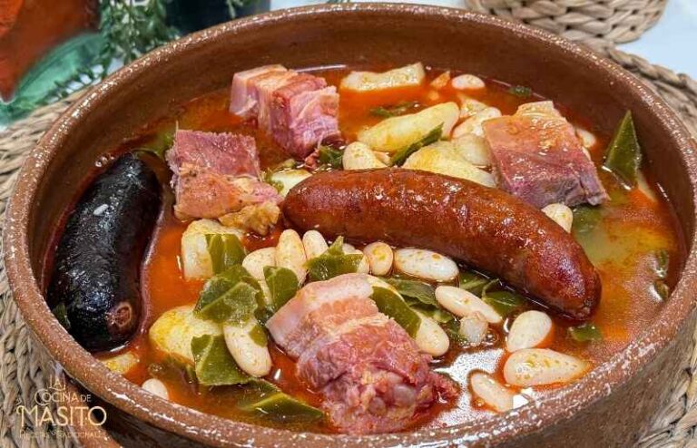 Un plato de pote asturiano servido en una cazuela de barro, con fabes, berza, patatas y embutidos ahumados.