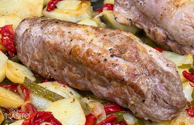 Plato de solomillo de cerdo al horno con patatas panaderas doradas y crujientes, acompañado de hierbas aromáticas.