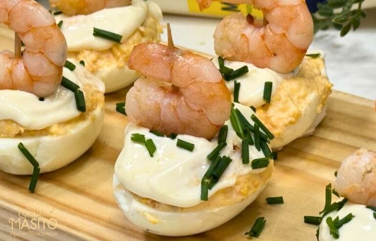 Huevos rellenos decorados con gambas al ajillo y perejil fresco sobre un plato blanco.