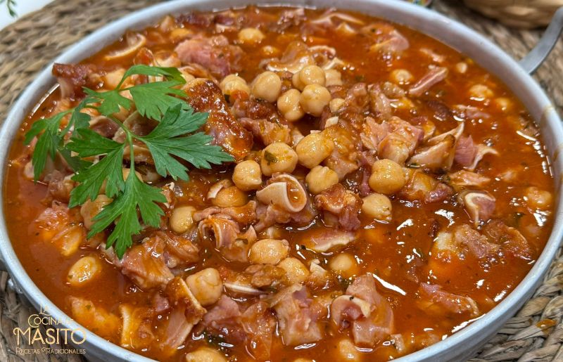 Plato de oreja en salsa con garbanzos servido en un cuenco, acompañado de pan crujiente y decorado con perejil fresco.