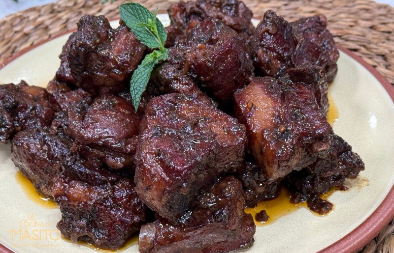 Costillas de cerdo melosas cocinadas en salsa de vino tinto, con un glaseado brillante y decoradas con una hoja de hierbabuena