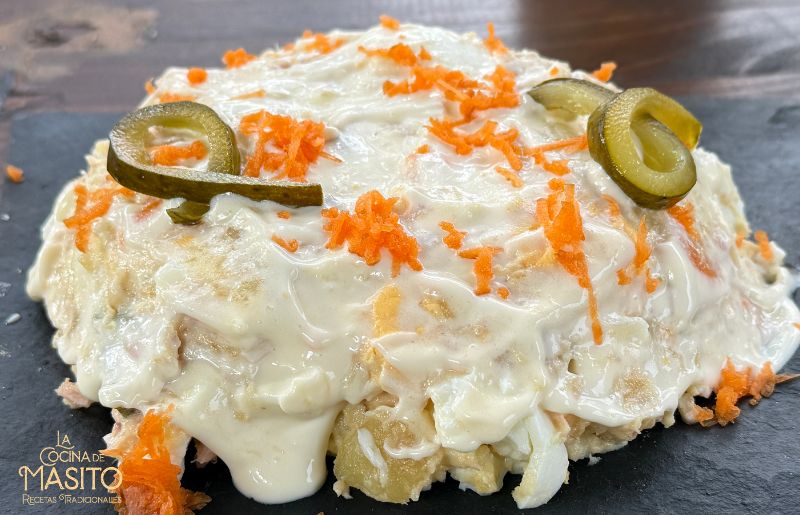 Ensaladilla de patatas asadas servida con pepinillo y zanahoria rallada.