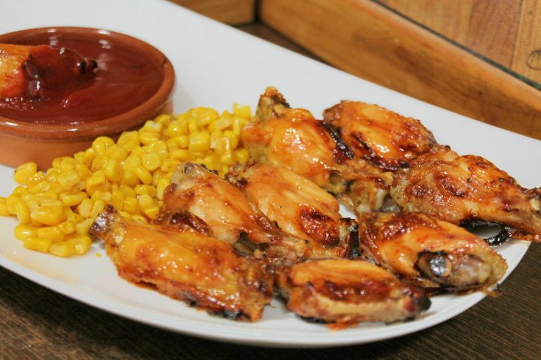 Alitas de pollo glaseadas con miel y kétchup, doradas al horno, servidas en un plato con un toque de pimienta